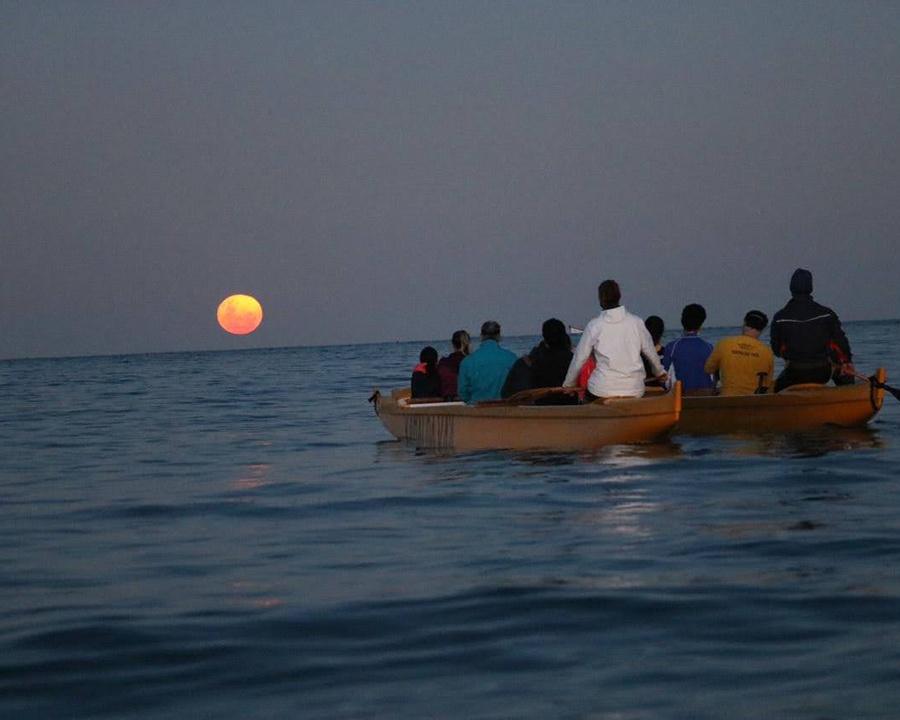 Praia ao pôr do sol com grupo de pessoas em barcos, atmosfera tranquila e relaxante em um cenário marítimo, ideal para viagens e experiências de lazer no litoral, Casa Maria Maria.